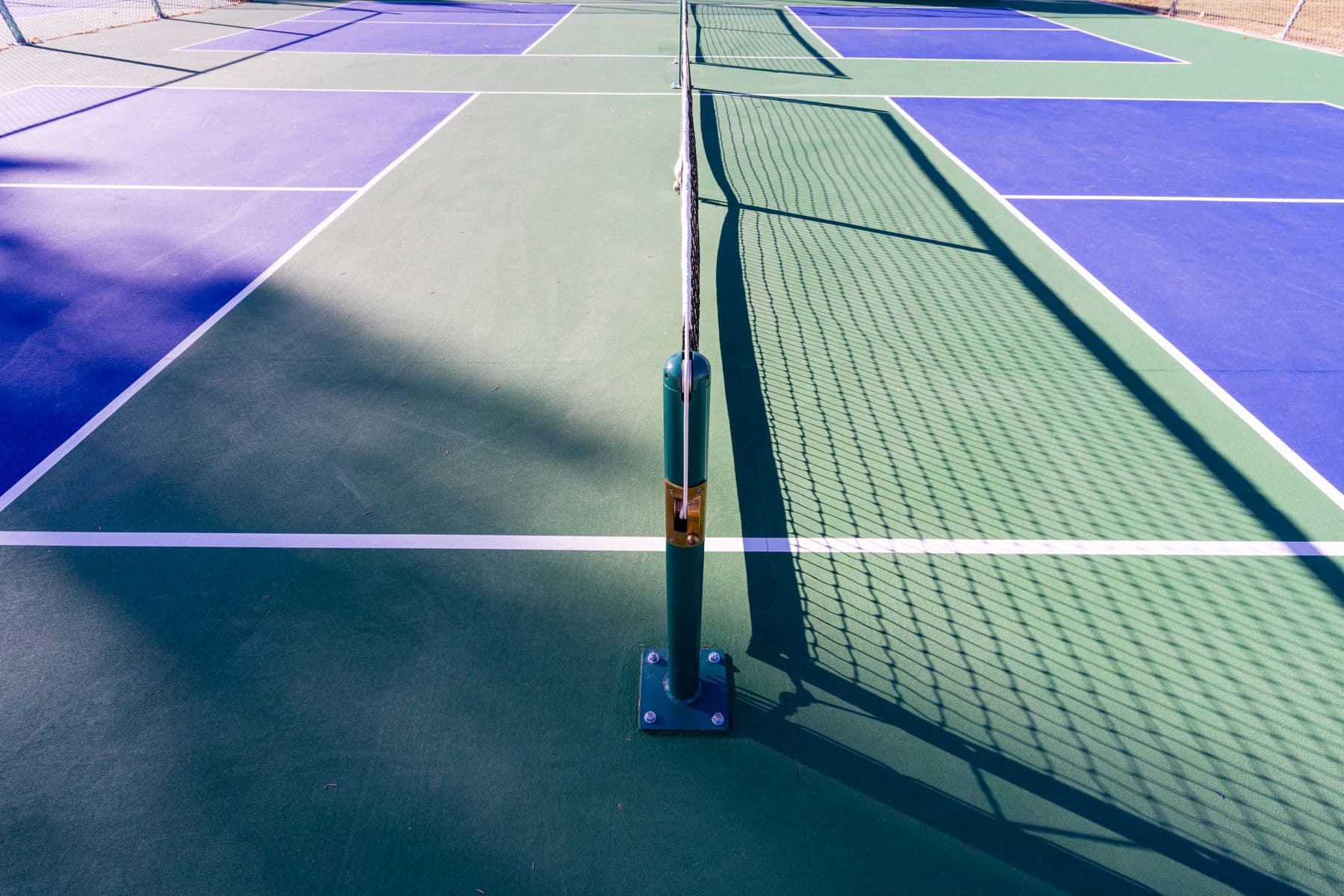 An empty outdoor pickleball court in sunlight, painted lines and a net, no players. Illustrative photo, not Lions Park itself.